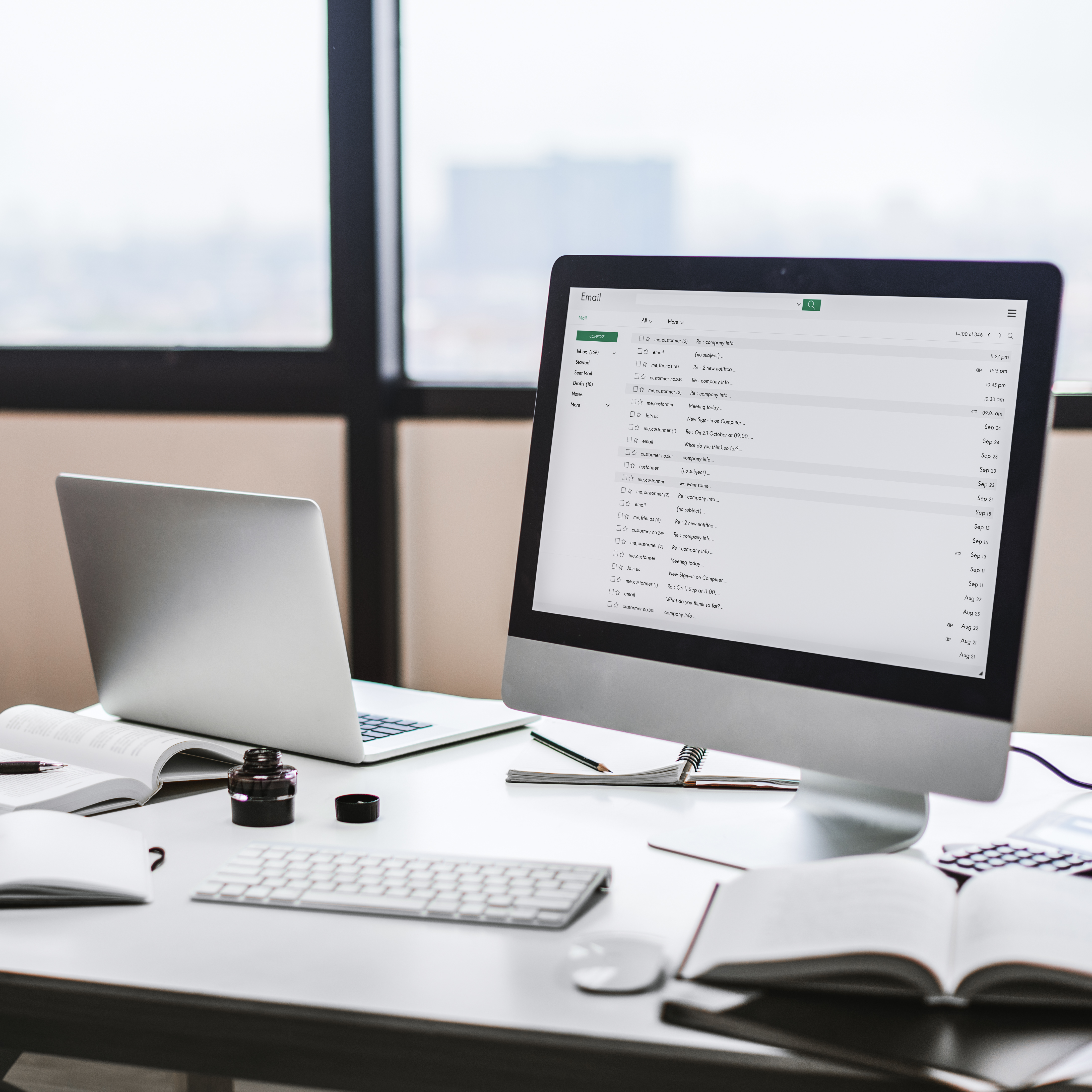 Workspace setup of an SEO agency in Kochi featuring a desktop computer displaying an email inbox, a laptop, notebooks, and office supplies near a large window with a city view.