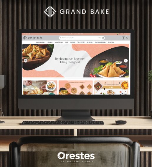 A realistic desktop mockup showcasing a modern e-commerce website design for Grand Bake on an iMac screen, presented in a corporate office setting with the Orestes Technologies Pvt. Ltd. logo at the bottom.
