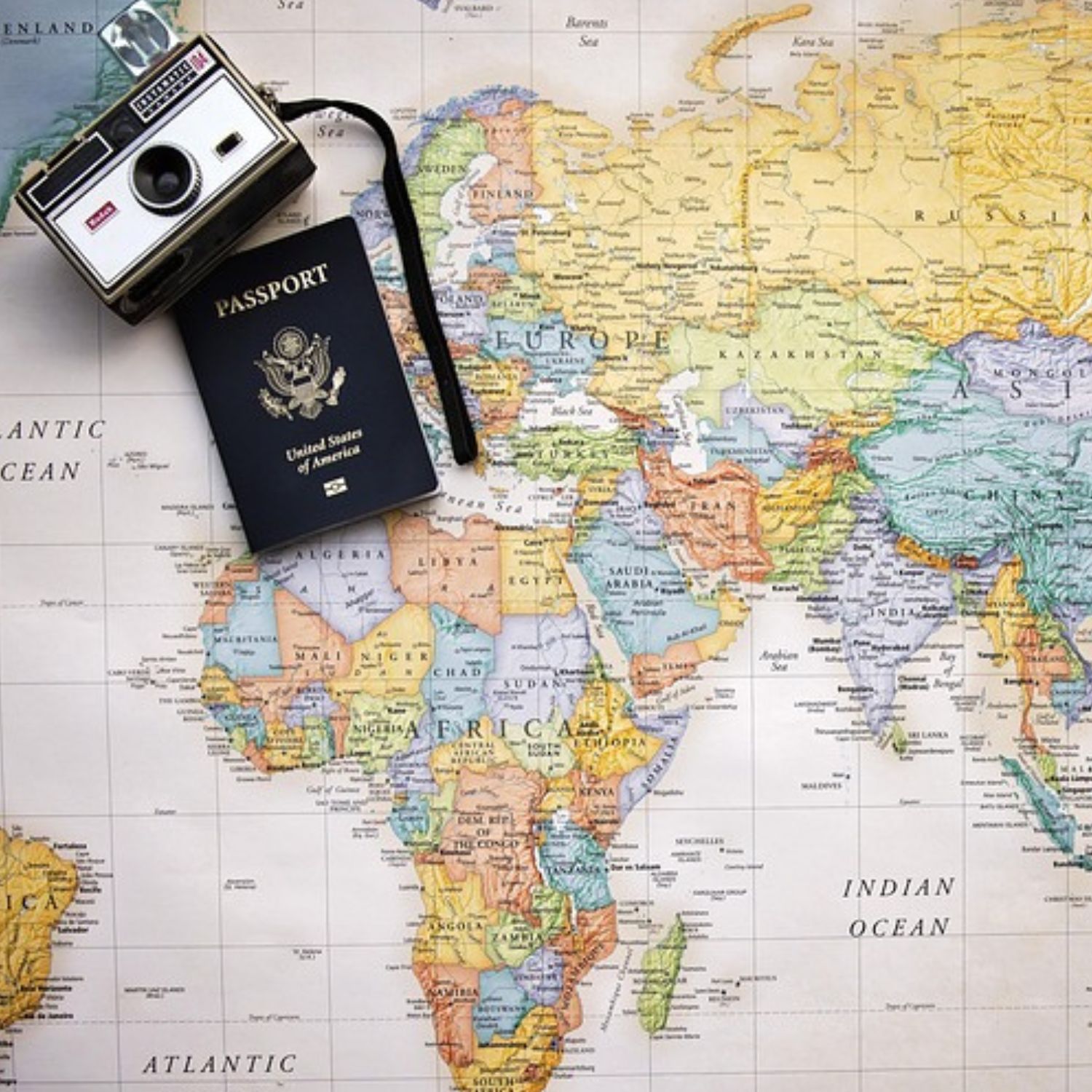 A United States passport and a vintage camera resting on a colorful world map, suggesting travel or trip planning.