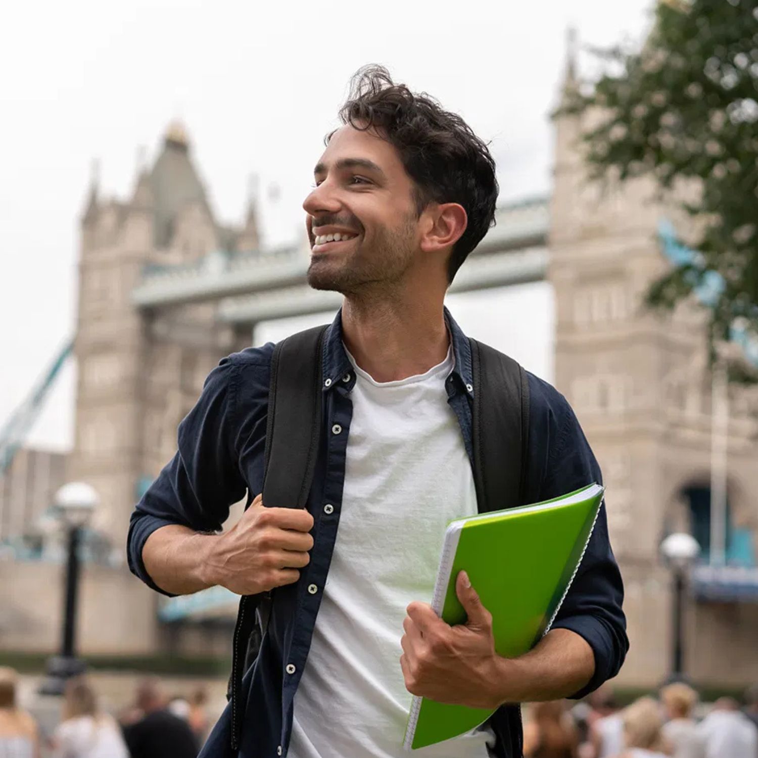 Happy student with a backpack and notebook standing near a historic architectural landmark, looking off into the distance with a smile